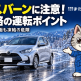 黒く凍結した冬の道路を走る車と、路面凍結への注意を案内するラチェットくん